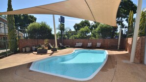 A swimming pool with a brick wall and lounge chairs under a canopy.