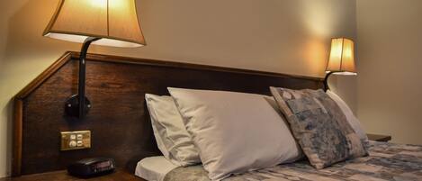 Habitación de hotel con cabecera de madera, mesita de noche con lámpara y cama con ropa de cama y almohadas estampadas.