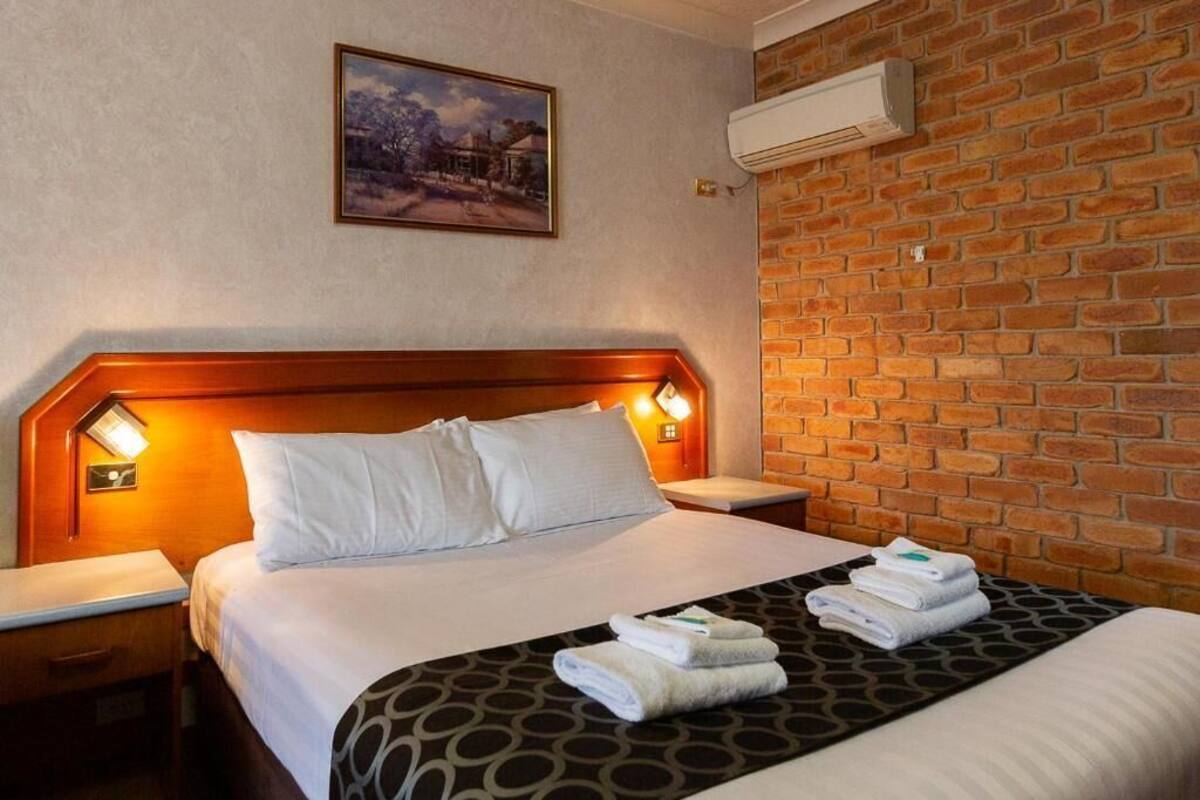 A hotel room with a brick wall, a wooden headboard, a painting, and a bed with towels.