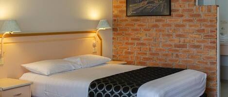 A hotel room with a brick wall, a bed with white bedding, two bedside lamps, and a framed picture on the wall.