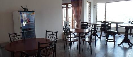 A dining area with multiple tables and chairs, a refrigerator, and a window with curtains.