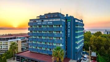 A multi-story hotel with balconies, a view of the sea, and a sunset in the background.