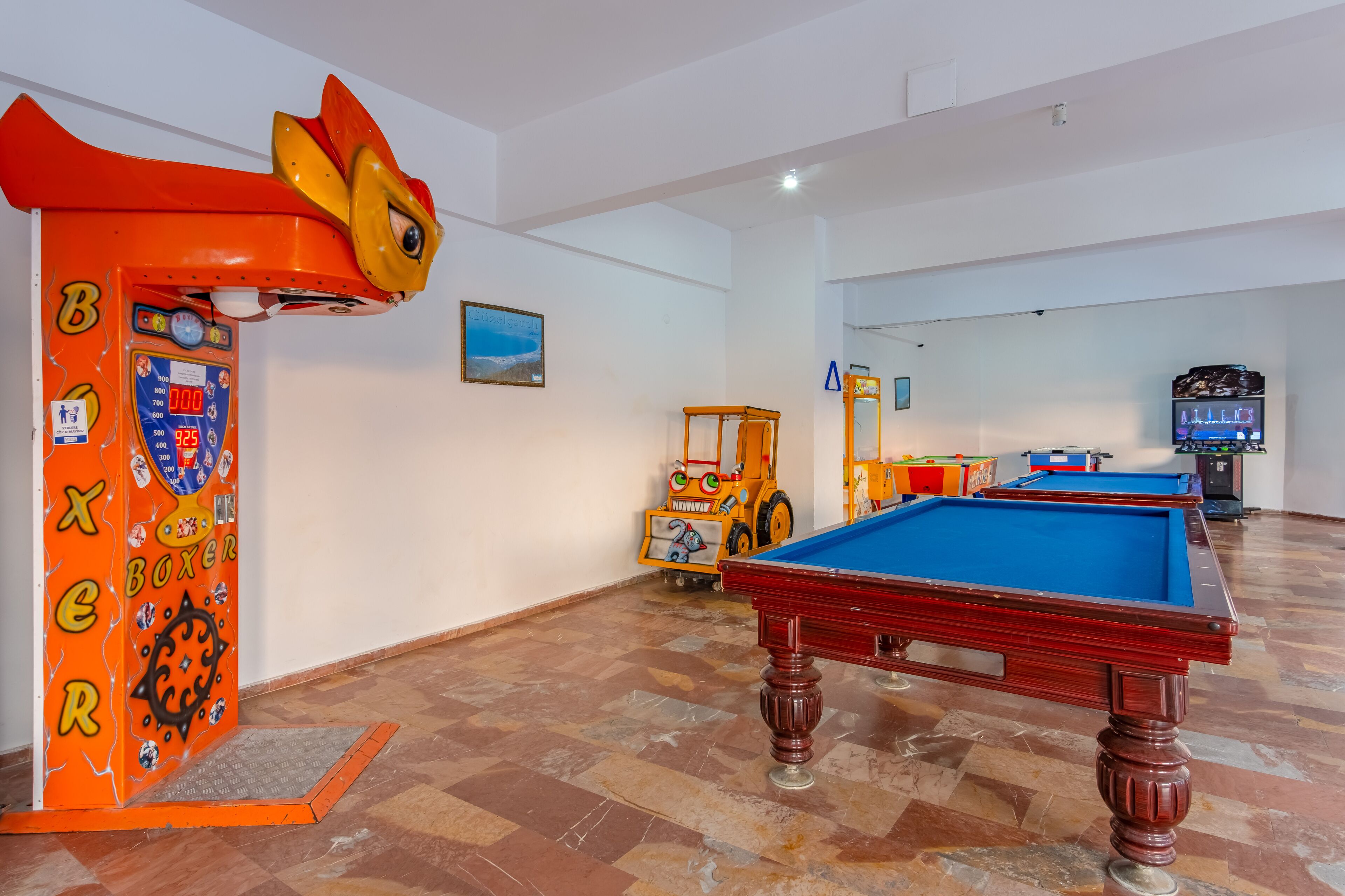 Una sala de billar con mesa de pool, un juguete para que jueguen los niños y una máquina recreativa de temática boxística.