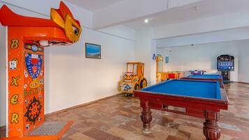 Una sala de billar con mesa de pool, un juguete para que jueguen los niños y una máquina recreativa de temática boxística.