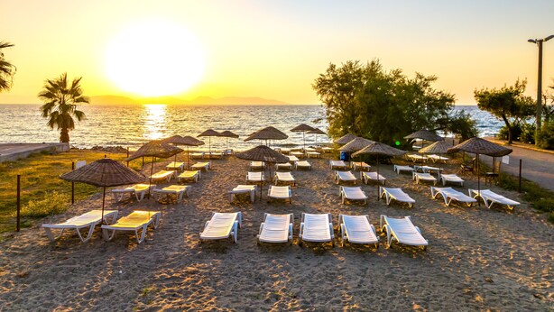 En strand med solstolar och parasoller som är uppställda för solbad.