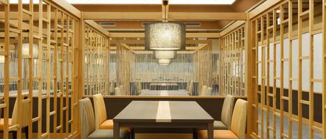 A modern dining area with a long table and chairs, wooden partitions, and a hanging light fixture.