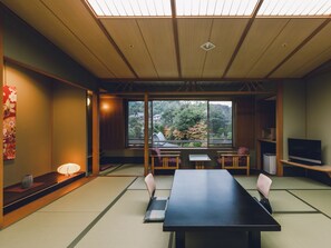 Une pièce de style japonais traditionnel, avec un sol recouvert de tatamis, une table basse, des chaises et un téléviseur.