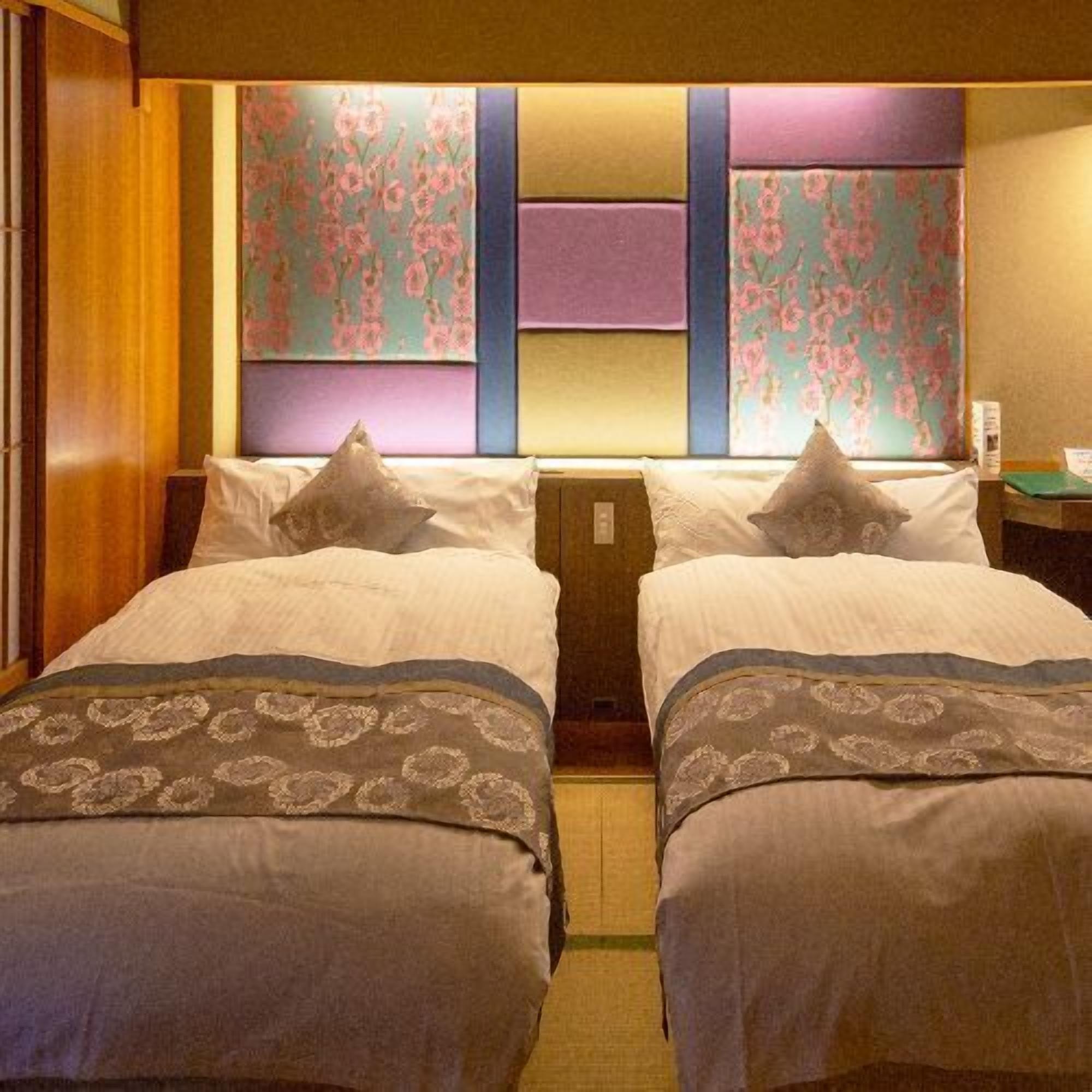 A hotel room with two beds, a wooden wardrobe, and a wall with a floral pattern.