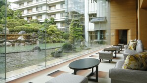 Een moderne hotellobby met een glazen wand met uitzicht op een vijver met koi karpers en begroeiing. Er zijn zithoeken met banken en tafels.