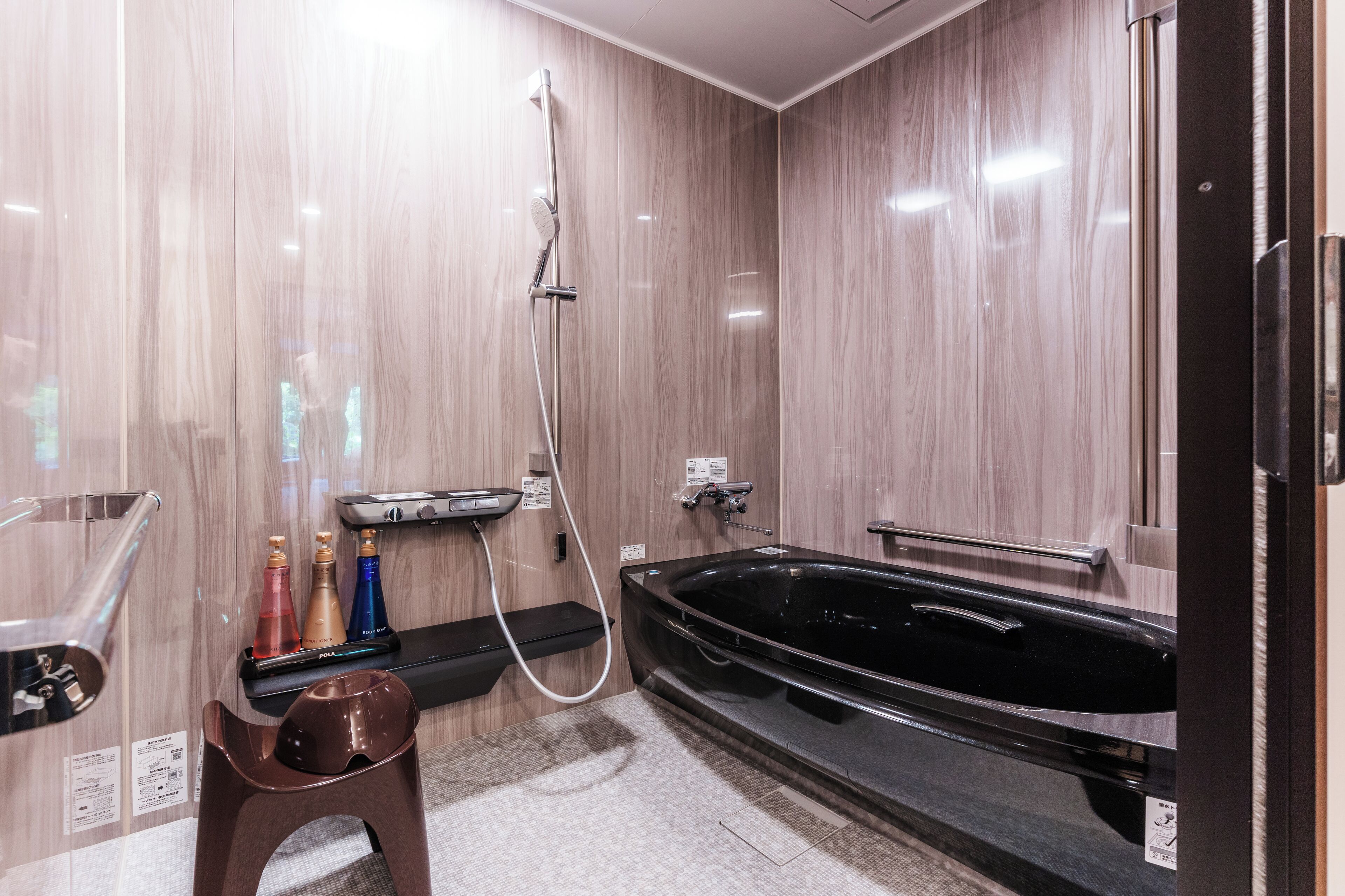 A modern bathroom with a black bathtub, a shower, and a small stool.