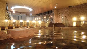 Een wellnesscentrum met een groot binnenzwembad, stenen muren en meerdere spiegels.