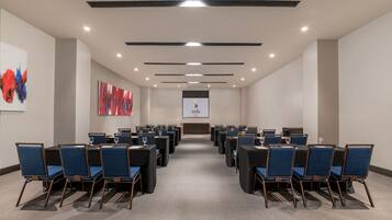 A conference room with rows of blue chairs, a projector screen, and abstract art on the walls.