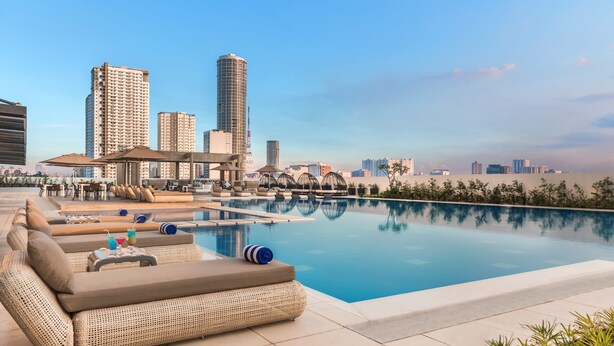 A rooftop pool area with lounge chairs, a bar, and a city skyline view.