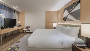 A hotel room with a large bed, a desk with a TV, a chair, and a lamp.