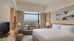 A hotel room with a large bed, a TV, a desk, a sofa, and a view of the city.