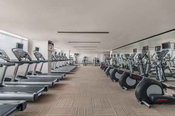 A gym with treadmills, elliptical machines, and stationary bikes arranged in rows.