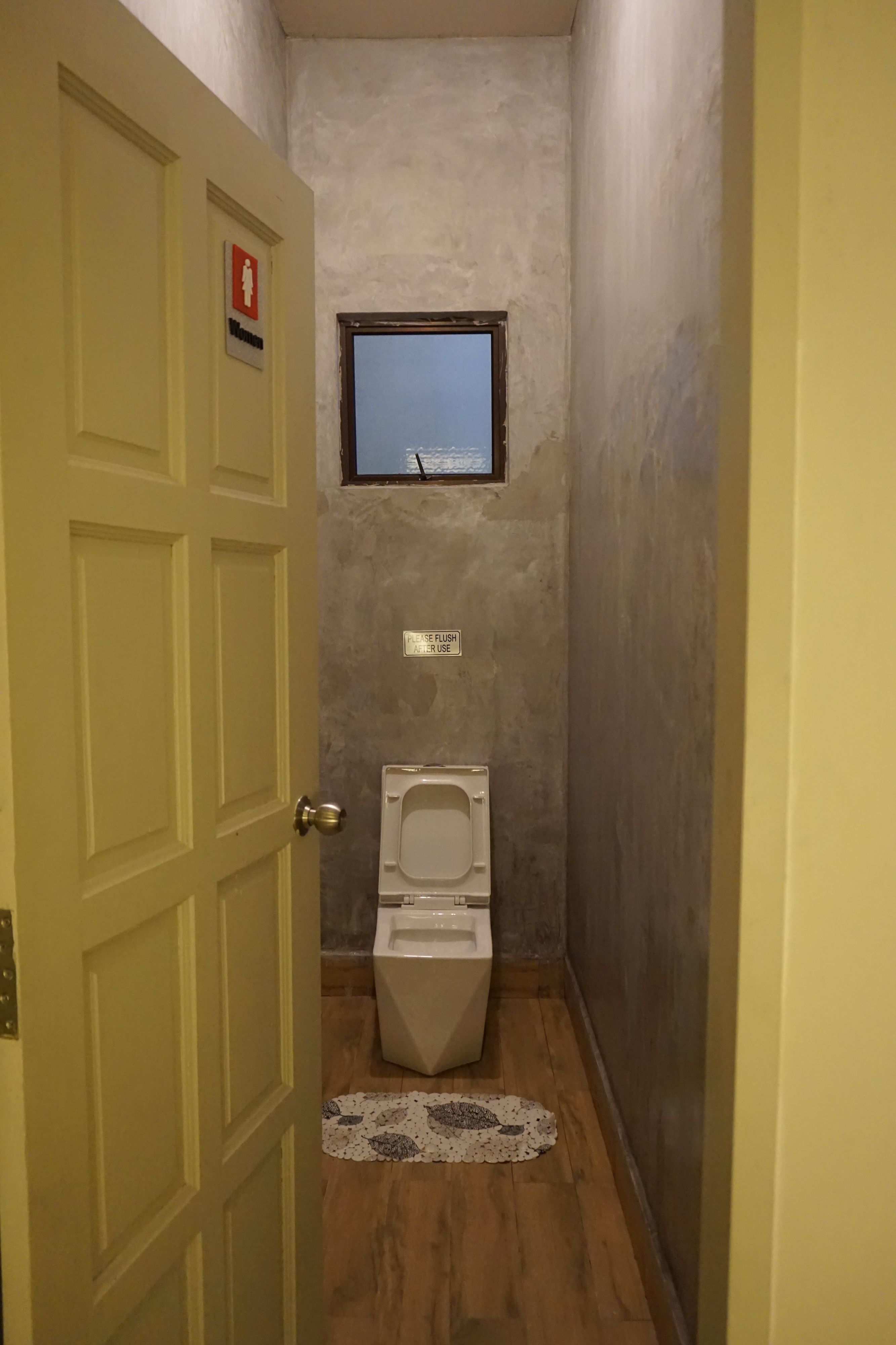 A narrow bathroom with a toilet, a window, and a door.
