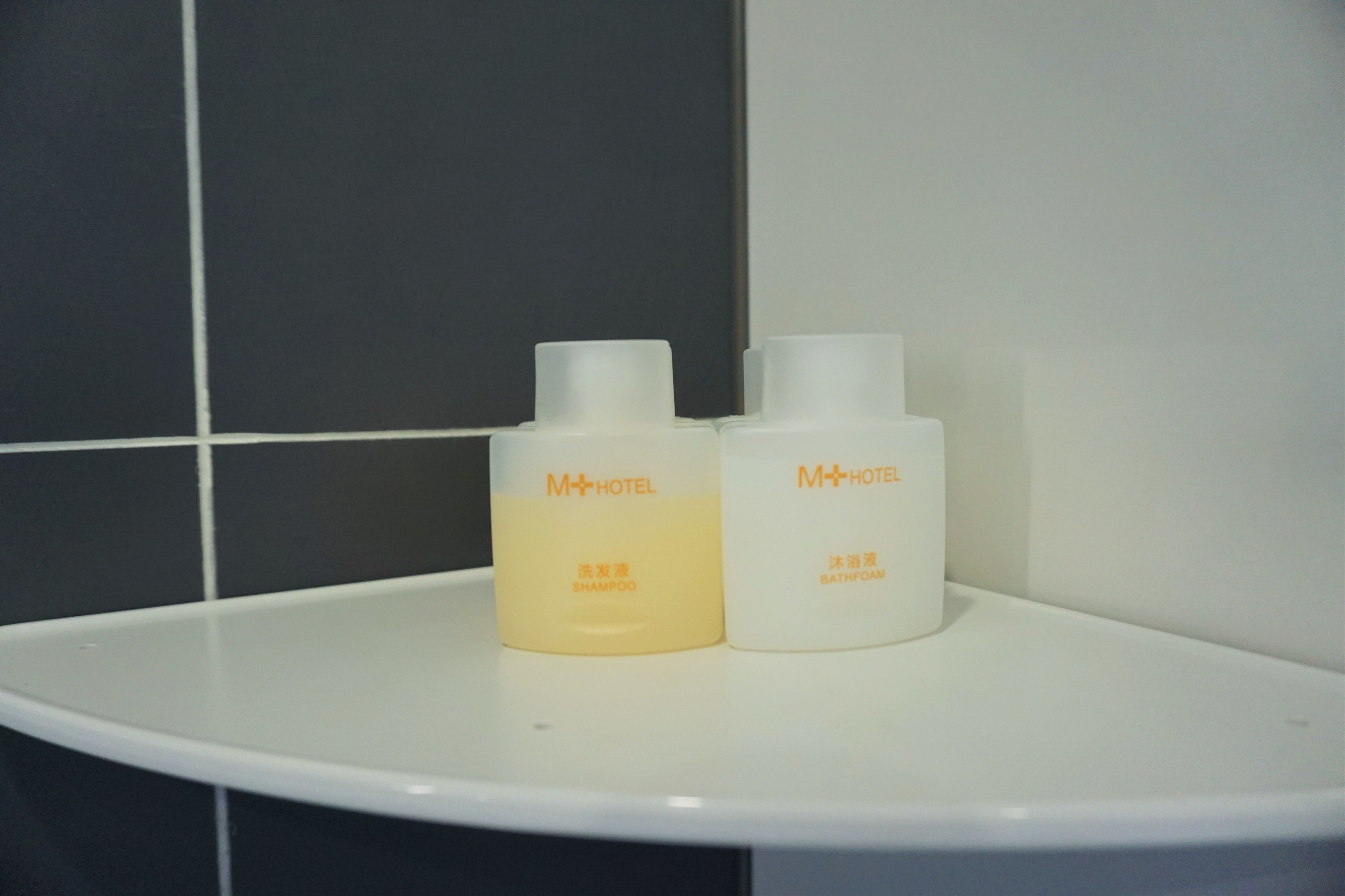 Two bottles of shampoo and bath foam on a white shelf against a tiled wall.
