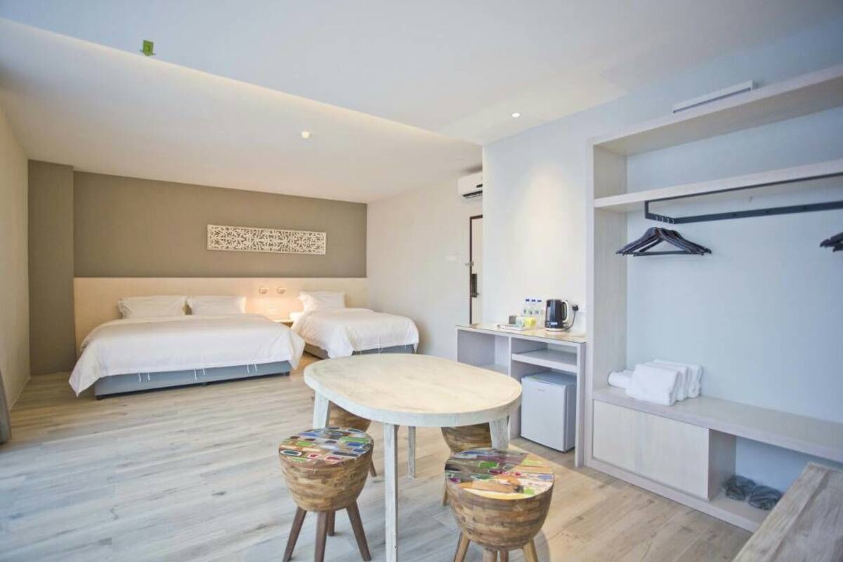 Ett modernt hotellrum med en stor säng, ett matbord, två pallar, ett litet pentry och en klädstång.