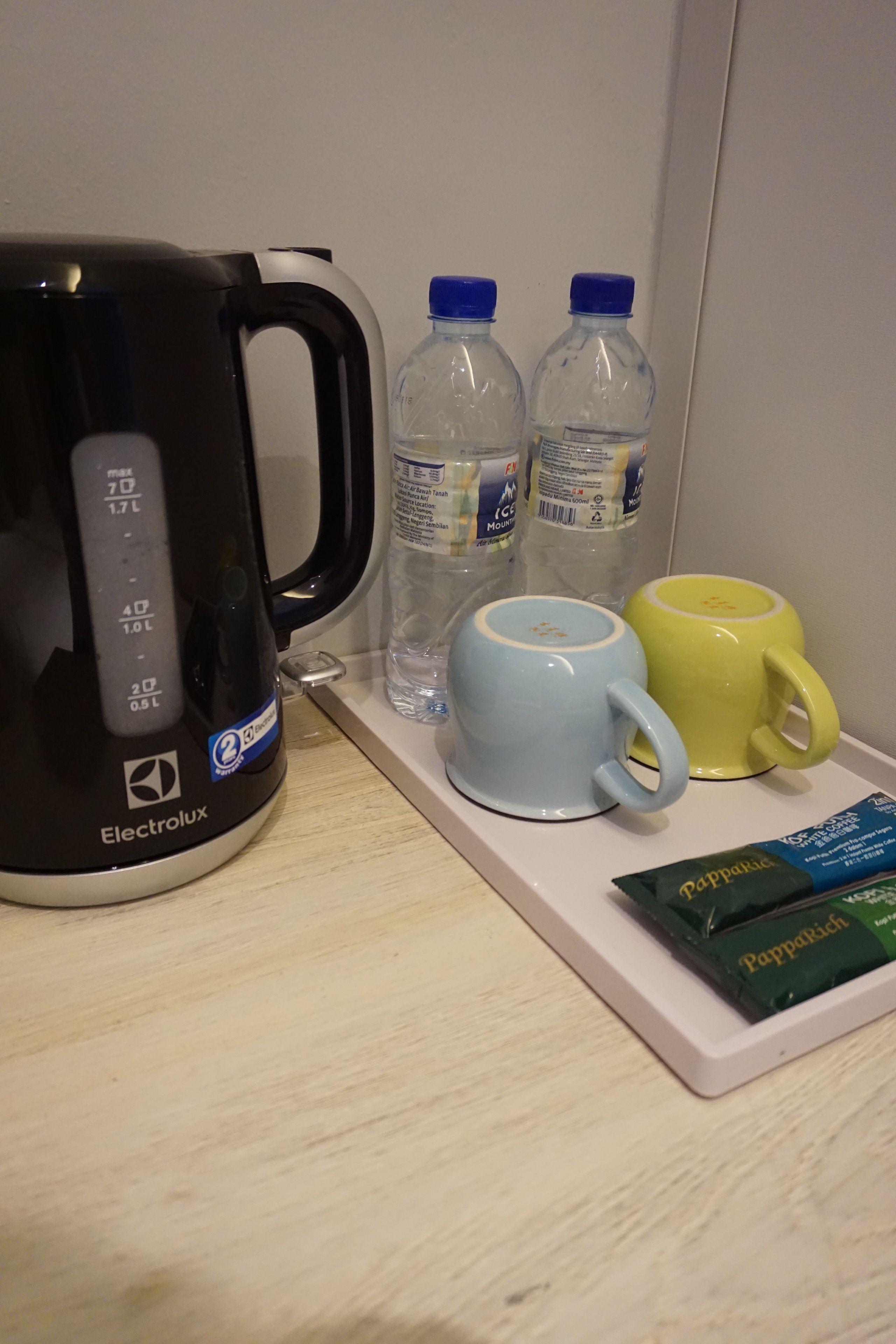 A kitchenette with an Electrolux coffee maker, two water bottles, a blue and a yellow mug, and a packet of Pappabich chocolate.