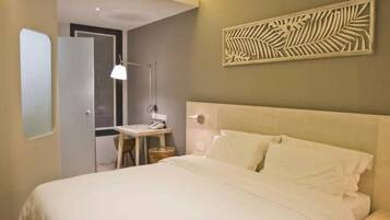 A hotel room with a large bed, a desk with a chair, a wall-mounted artwork, and a door leading to another room.