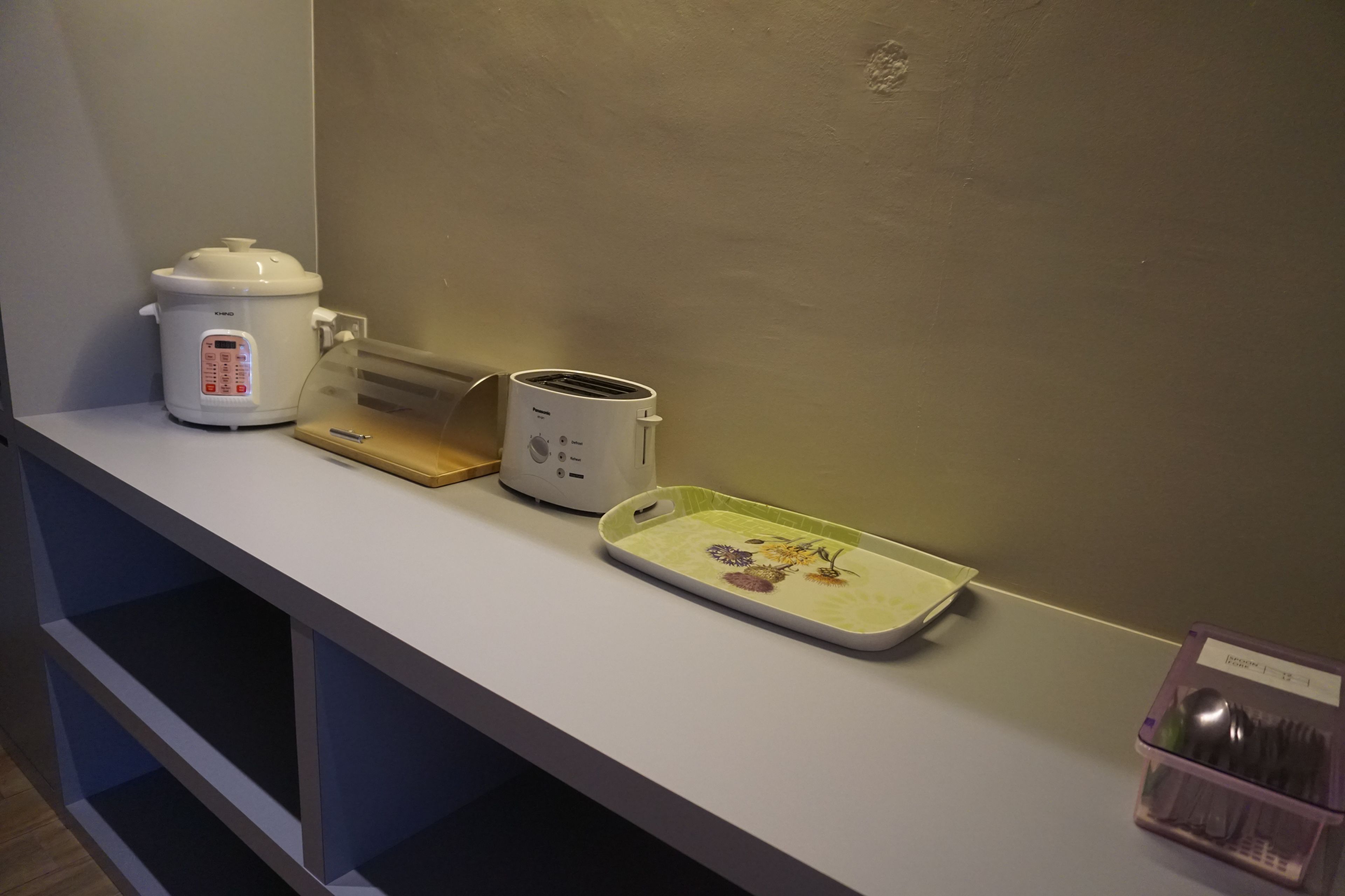 A kitchen counter with a slow cooker, toaster, and a tray with utensils.
