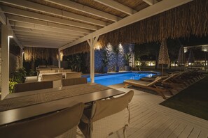 An outdoor pool area with lounge chairs and tables, surrounded by potted plants and a stone wall. - Sandal Alaçatı - Adults Only (Cesme)