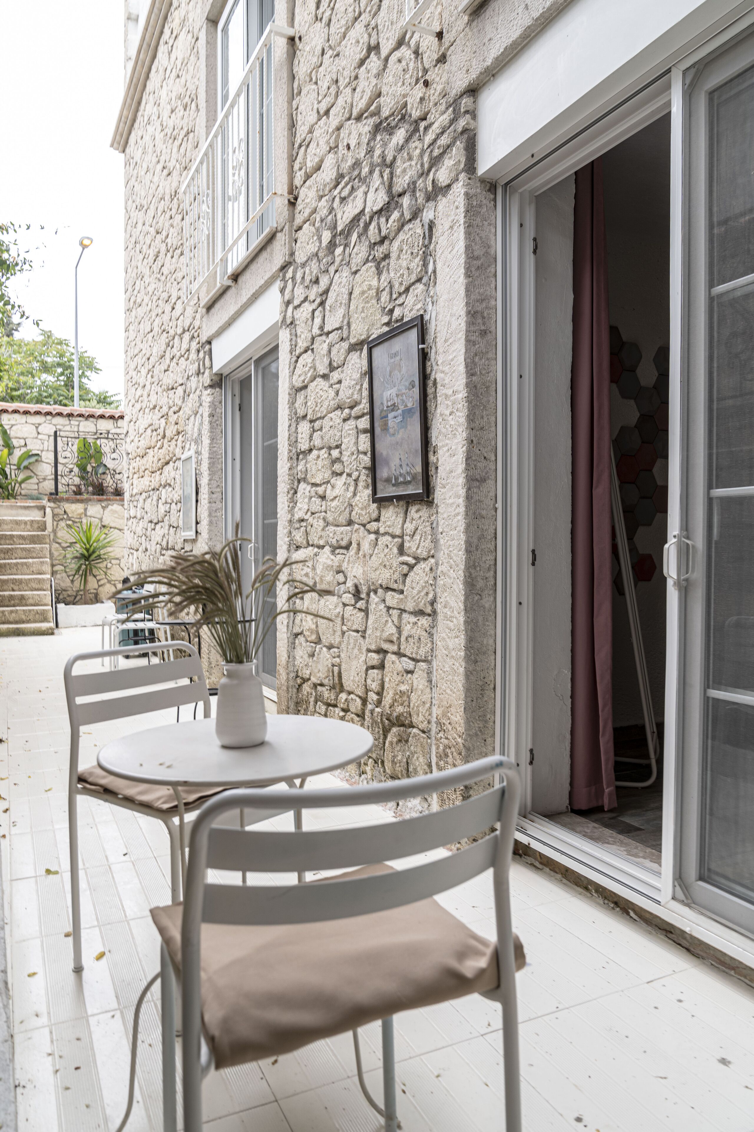 A stone building with a patio area featuring a round table and chairs, a potted plant, and a door with a curtain.