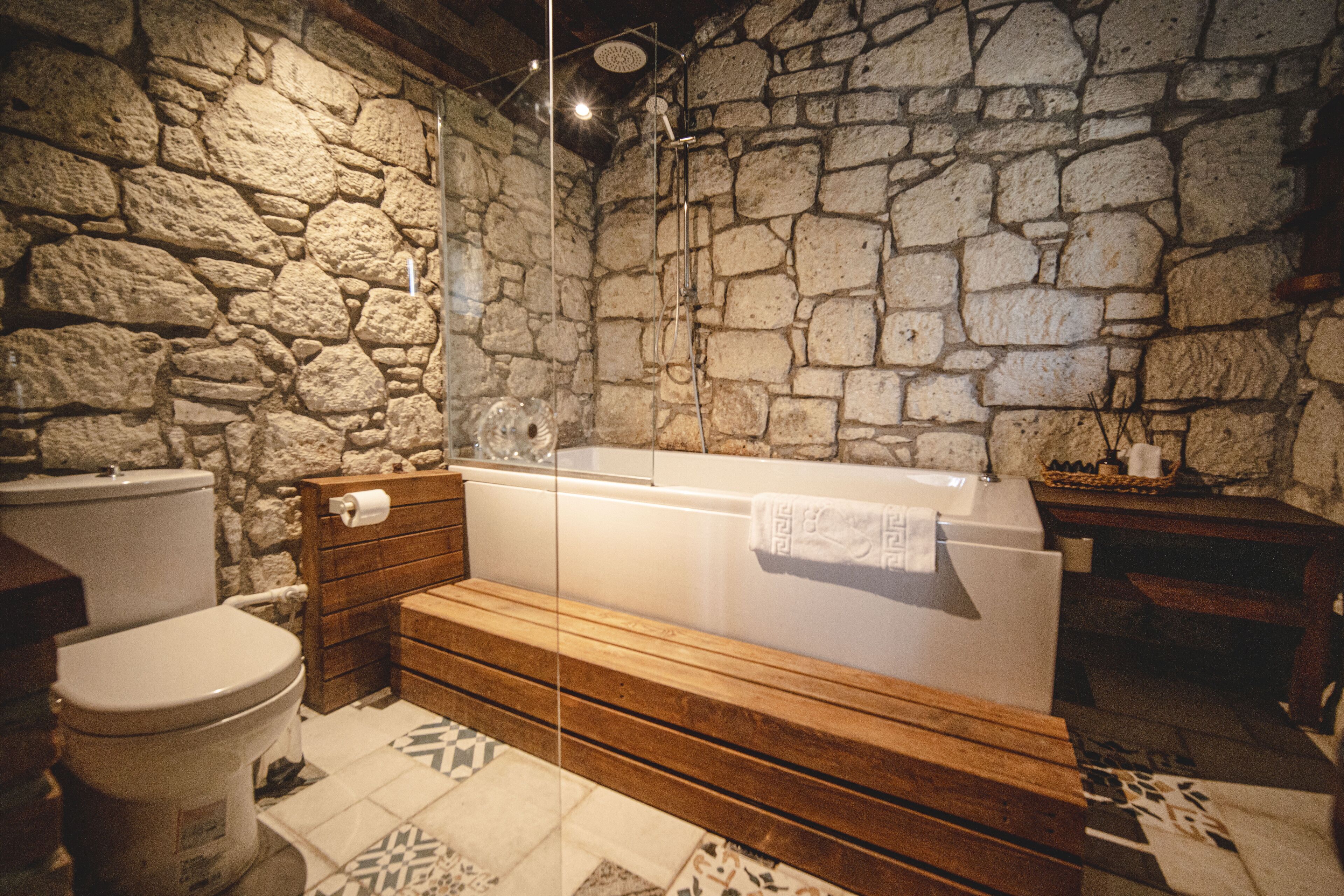 A bathroom with a stone wall, a wooden bench, a bathtub, and a toilet.