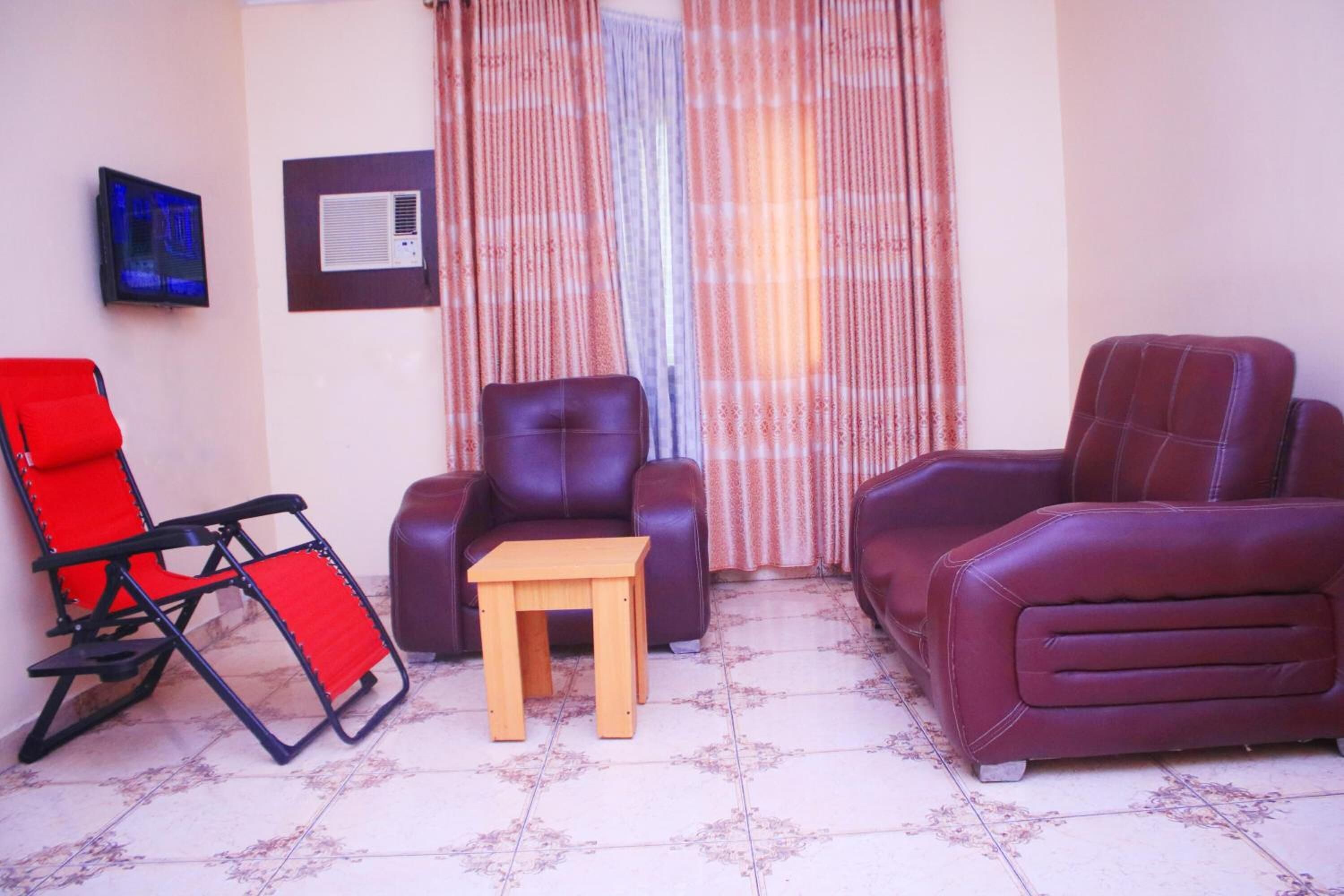 A living room with a red folding chair, a brown leather sofa, a wooden coffee table, and a television mounted on the wall.