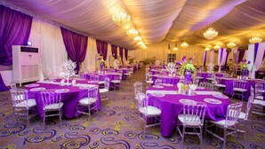 A banquet hall with round tables covered in purple tablecloths, clear chairs, and chandeliers. - Agburuike Hotels (Aba)