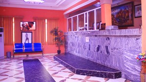 A lobby with a marble reception desk, blue seating area, and a large painting on the wall. - Agburuike Hotels (Aba)