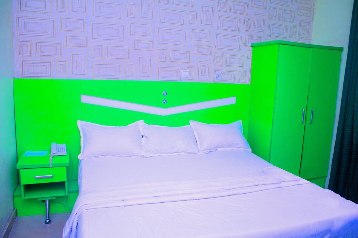 A room with a green headboard, white bedding, a green nightstand with a phone, and a green wardrobe.