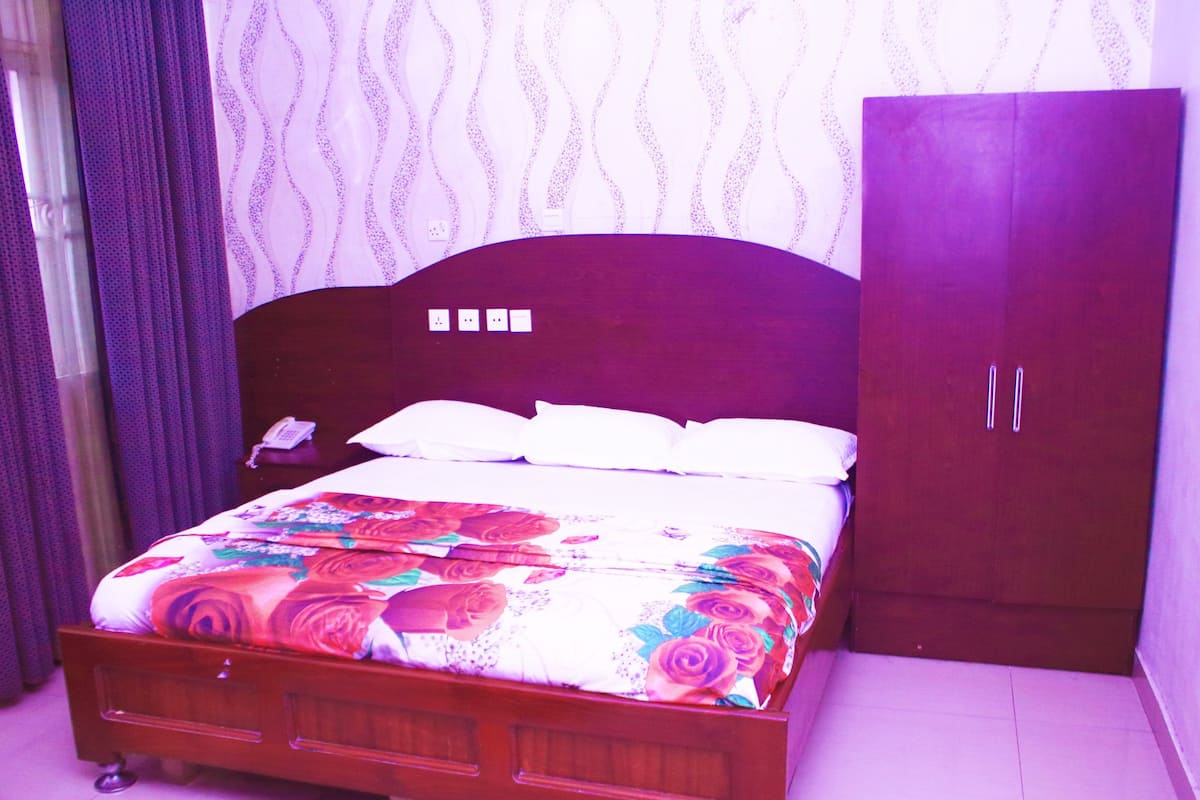 A bedroom with a wooden bed, white bedding, a telephone, and a wardrobe.