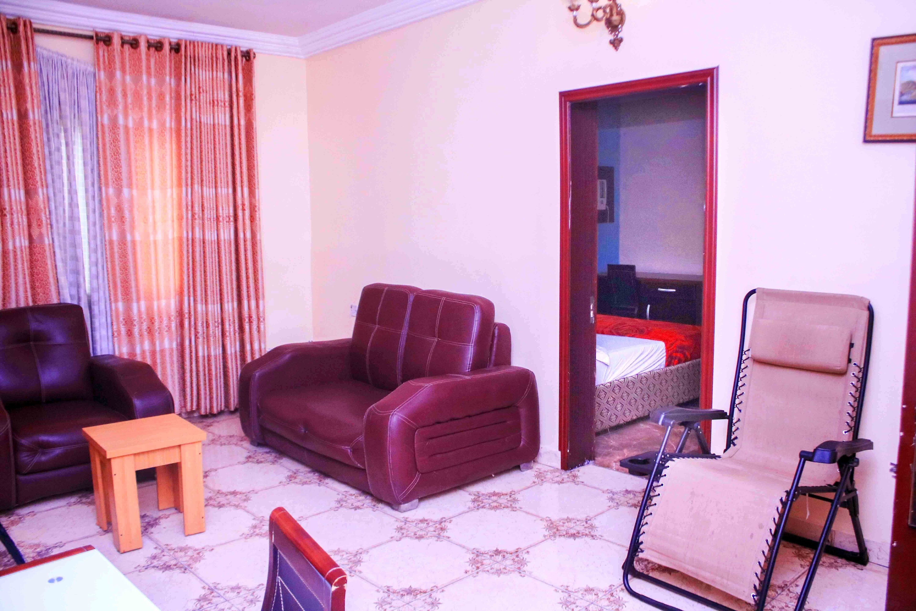 A living room with a brown sofa, a wooden table, a beige armchair, and a patterned floor.