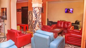 A lobby with red and blue seating, a television, and a patterned pillar. - Agburuike Hotels (Aba)