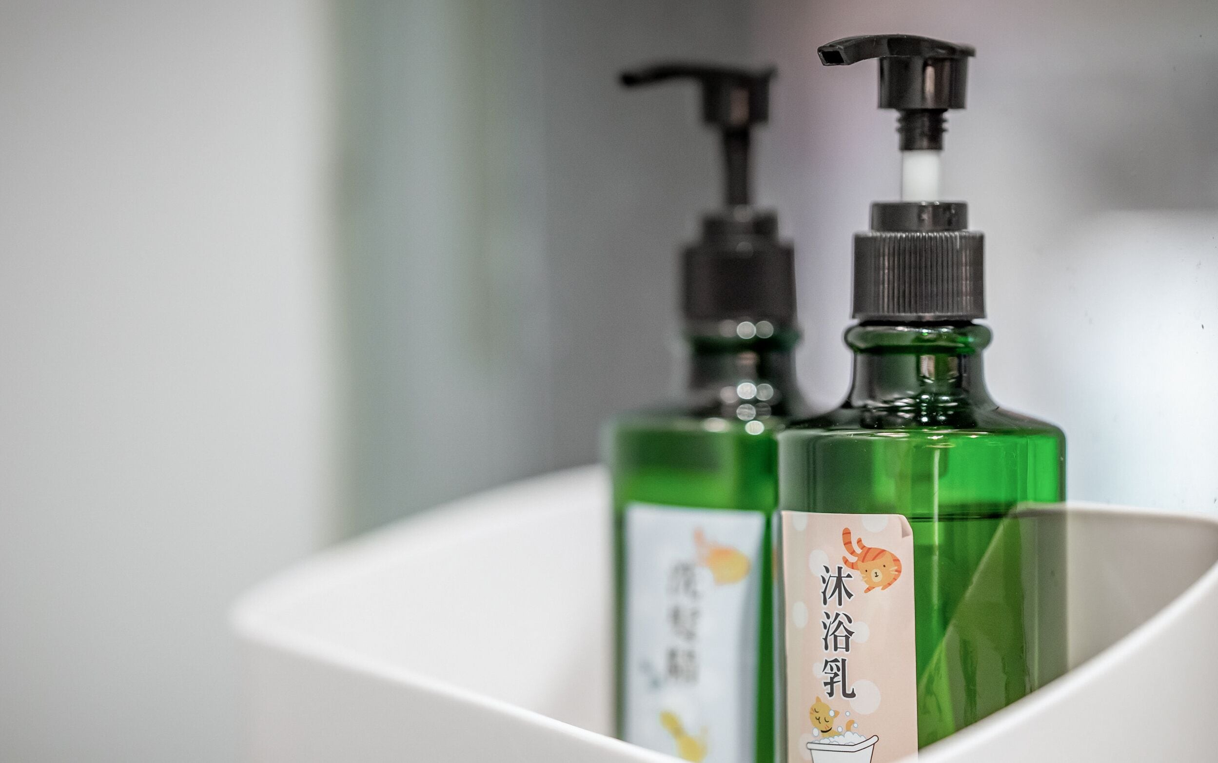 Dos botellas verdes con dispensadores negros en un lavabo blanco.