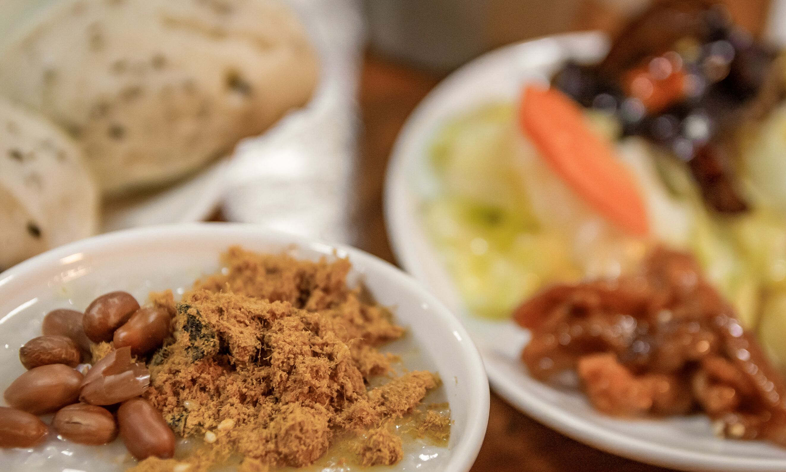 A table with various dishes including beans, a bowl of a crumbly substance, and a plate with vegetables and meat.