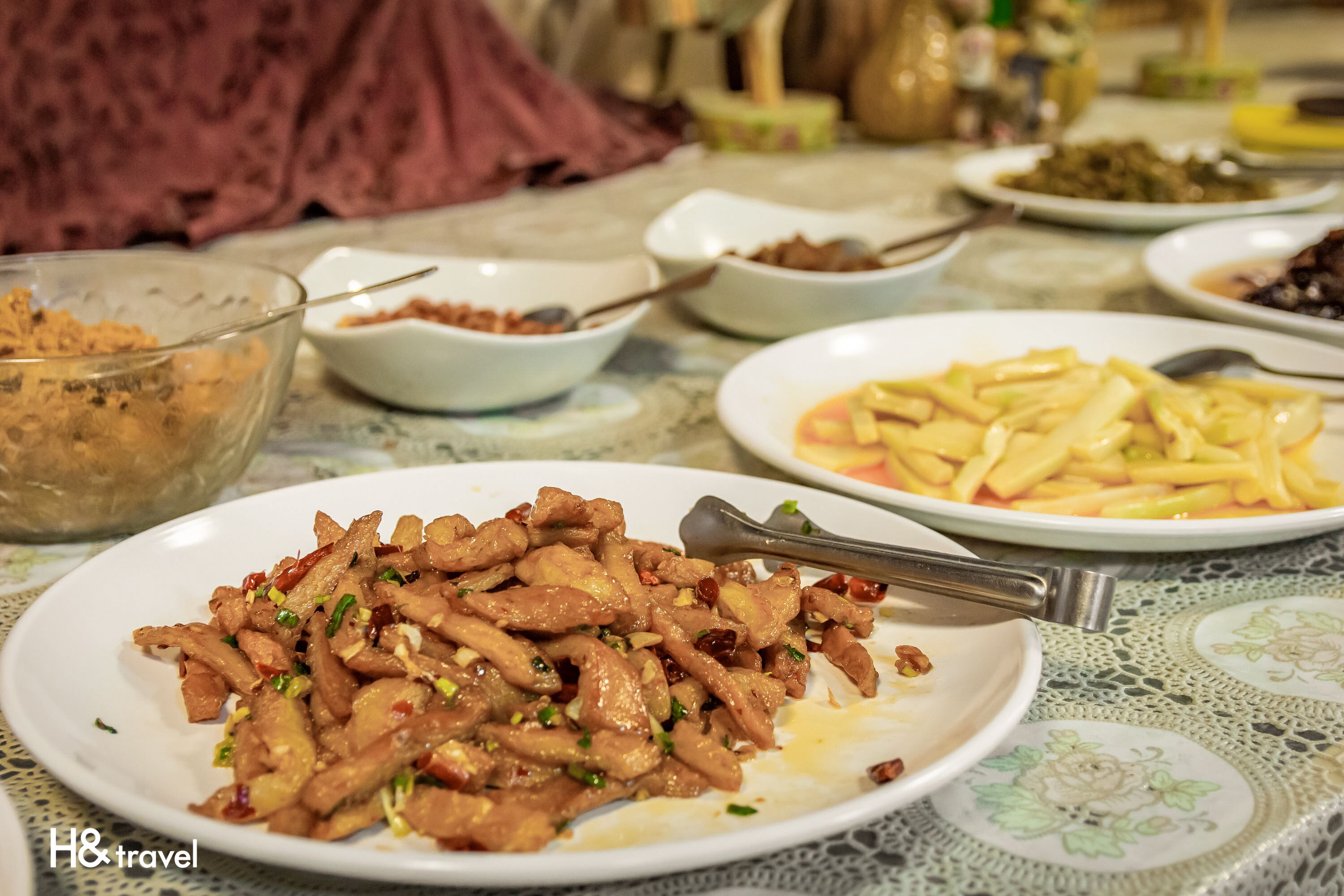 A table with various dishes, including a plate of stir-fried meat, a bowl of soup, and other food items.