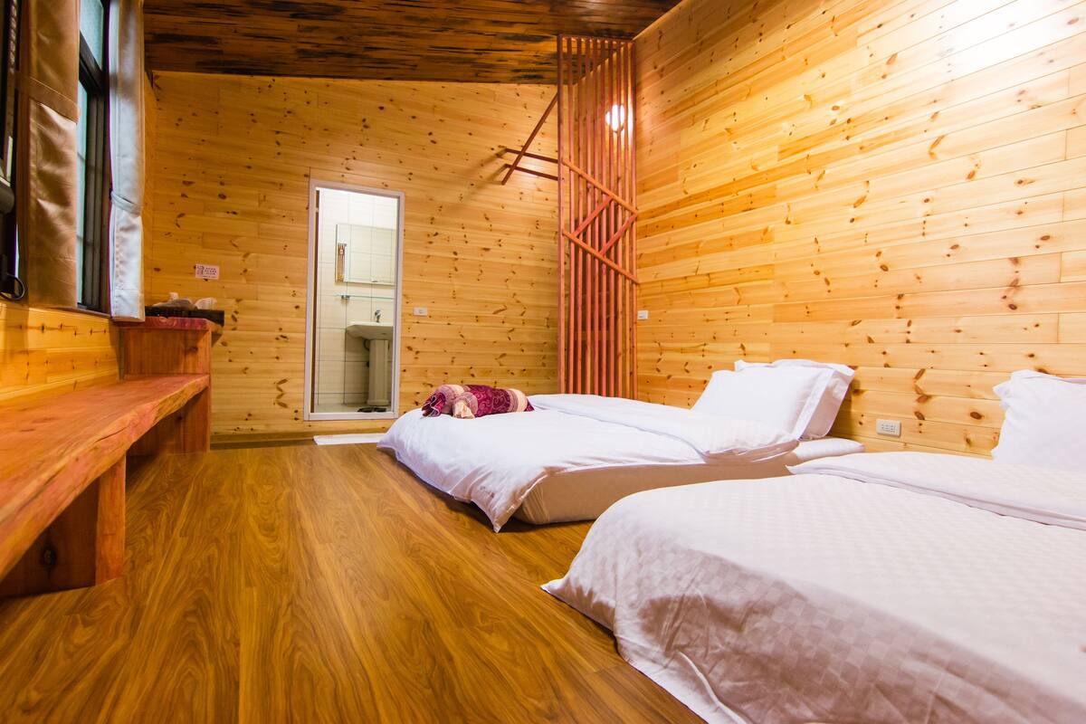 Una habitación tipo cabaña de madera con dos camas, un banco y piso de madera.