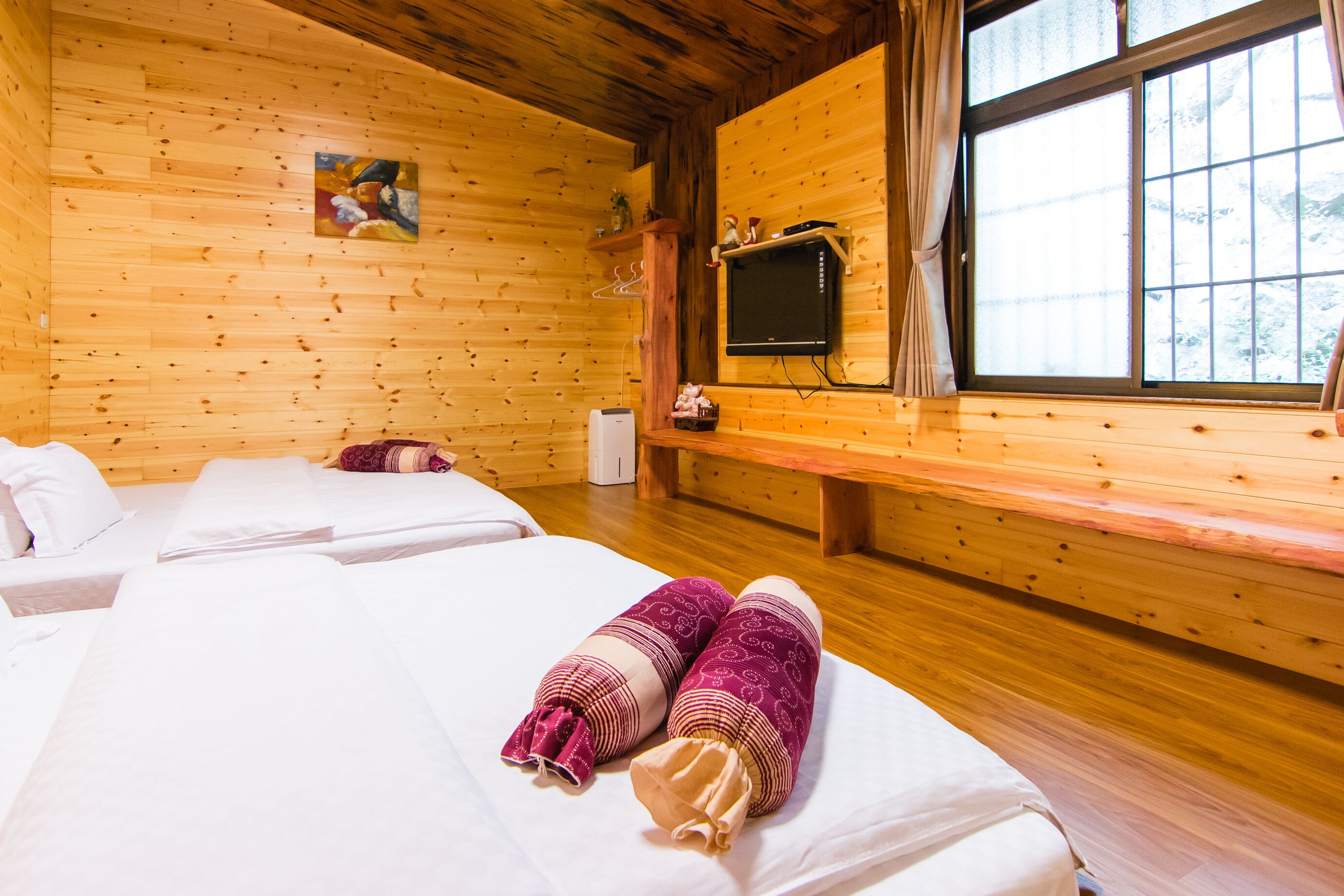 A wooden cabin room with two beds, a television, and a window with a view.