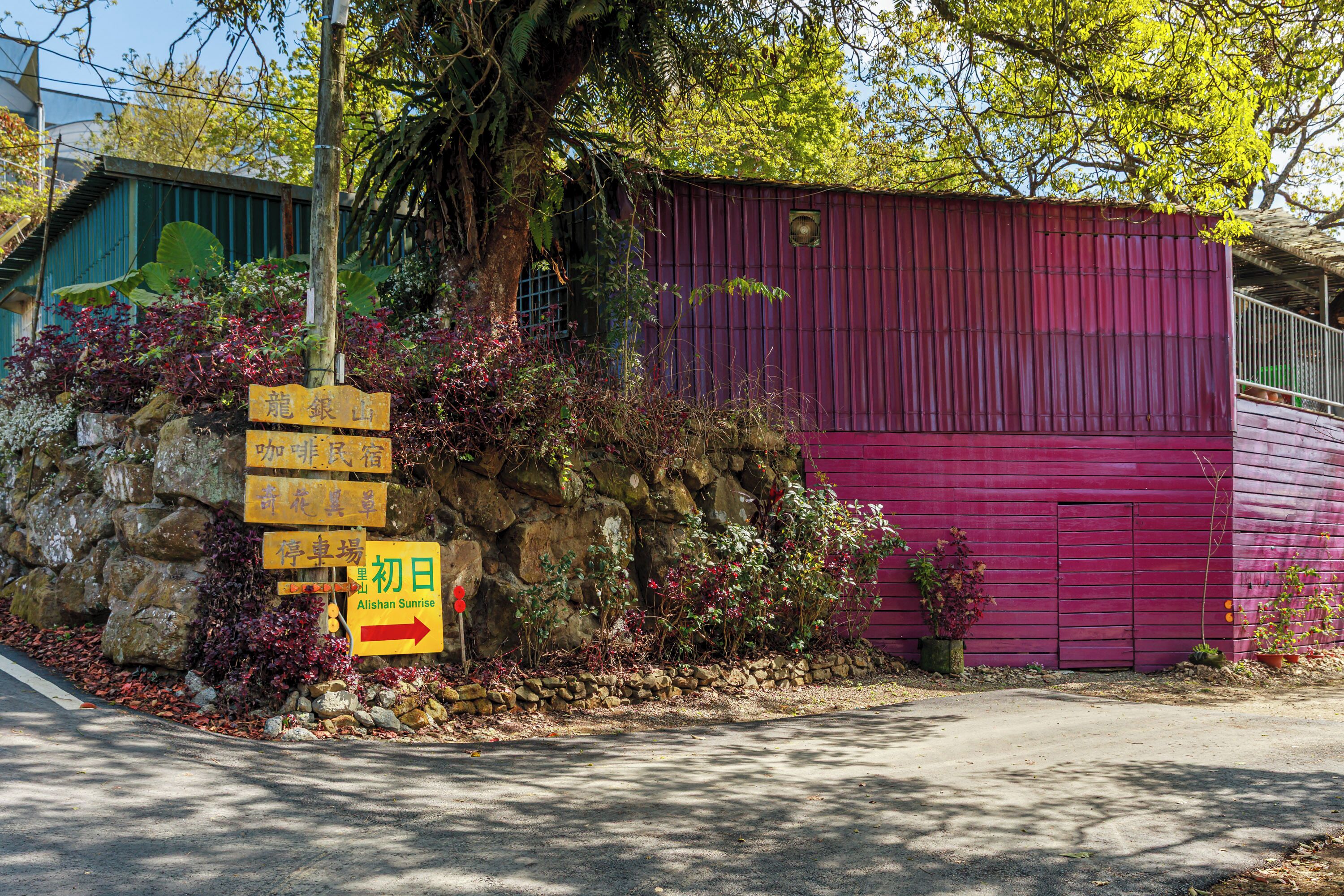 A building with a red exterior, a stone wall with plants, and multiple directional signs.