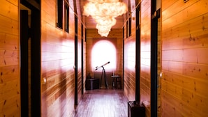 Un estrecho pasillo de madera con un telescopio y un taburete, que conduce a una ventana circular y luminosa.