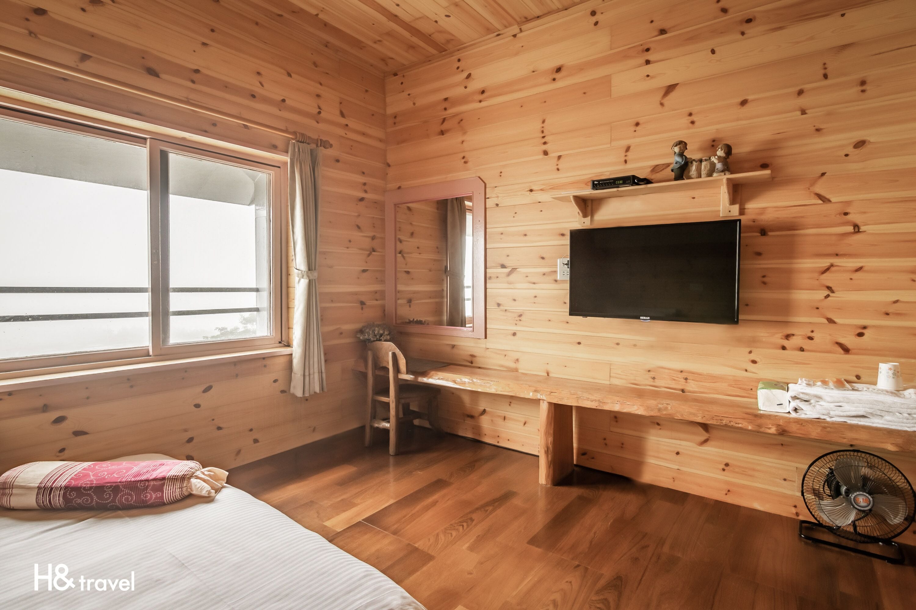 Une chambre dans un chalet en bois, comprenant un lit, un bureau, une chaise, une télévision et un ventilateur.
