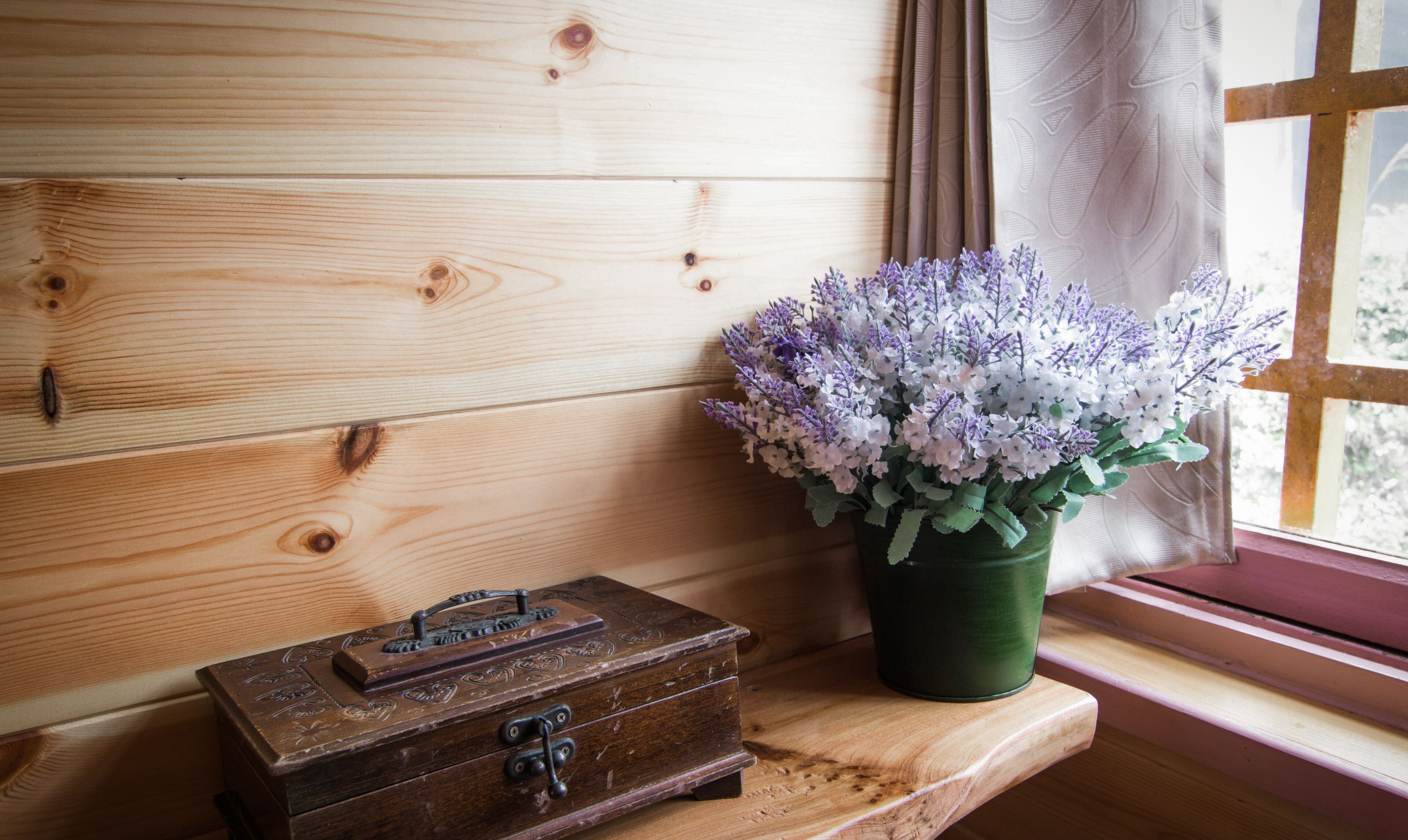A wooden chest with a lock on a window sill, next to a vase of flowers.