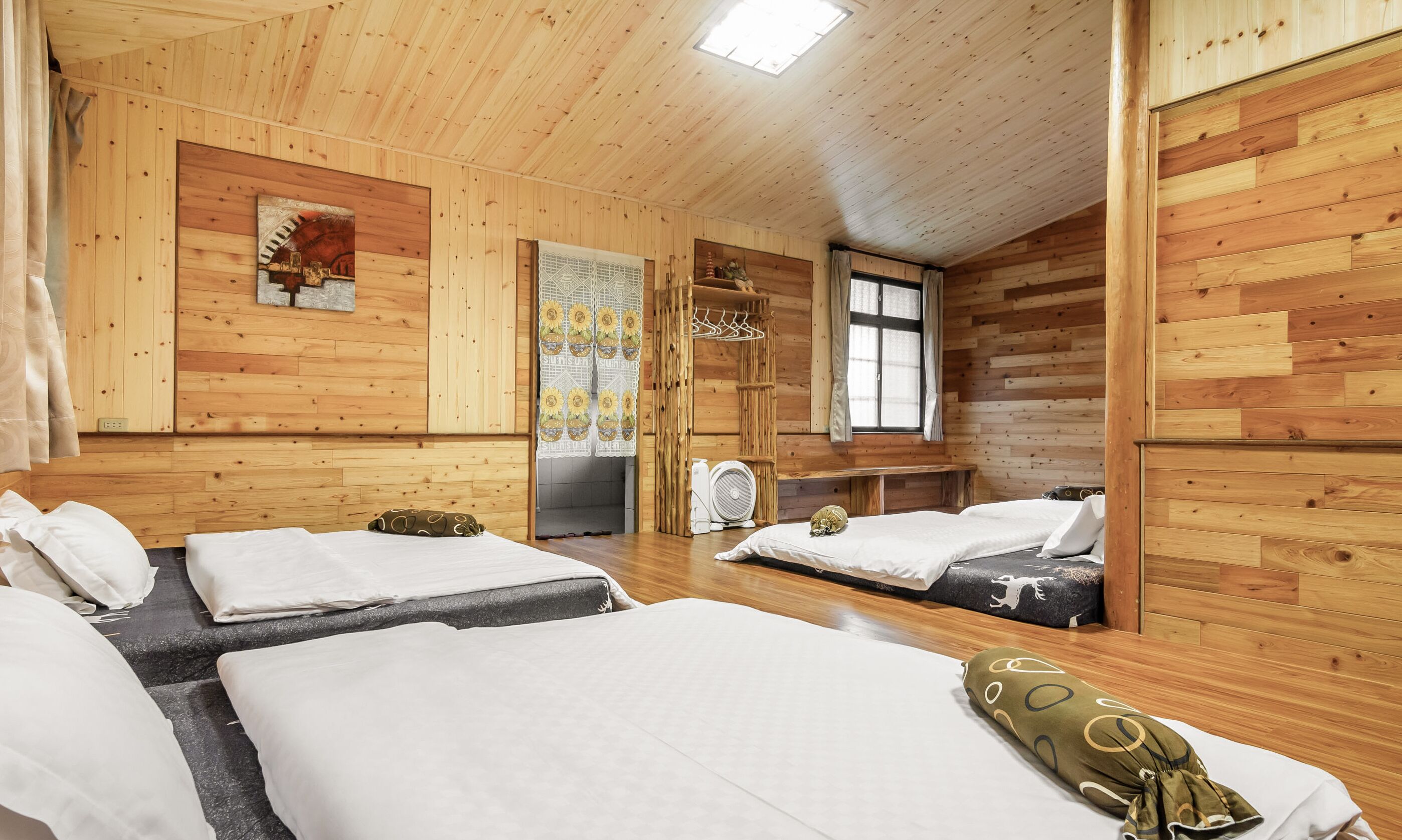 Habitación de cabaña de madera con tres camas, un banco y un ventilador.