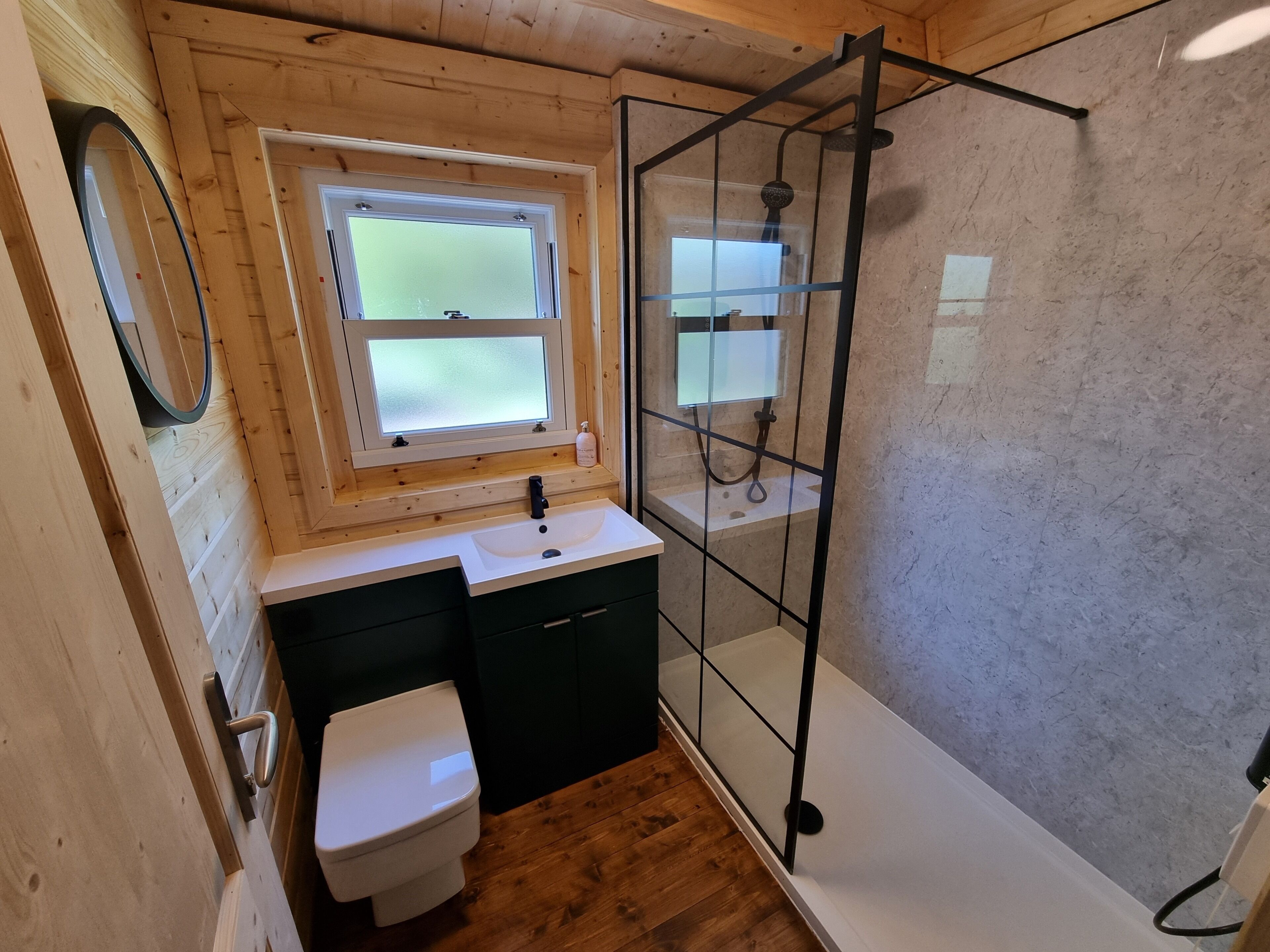 A compact bathroom with a wooden interior, a white sink, a toilet, and a glass-enclosed shower area.