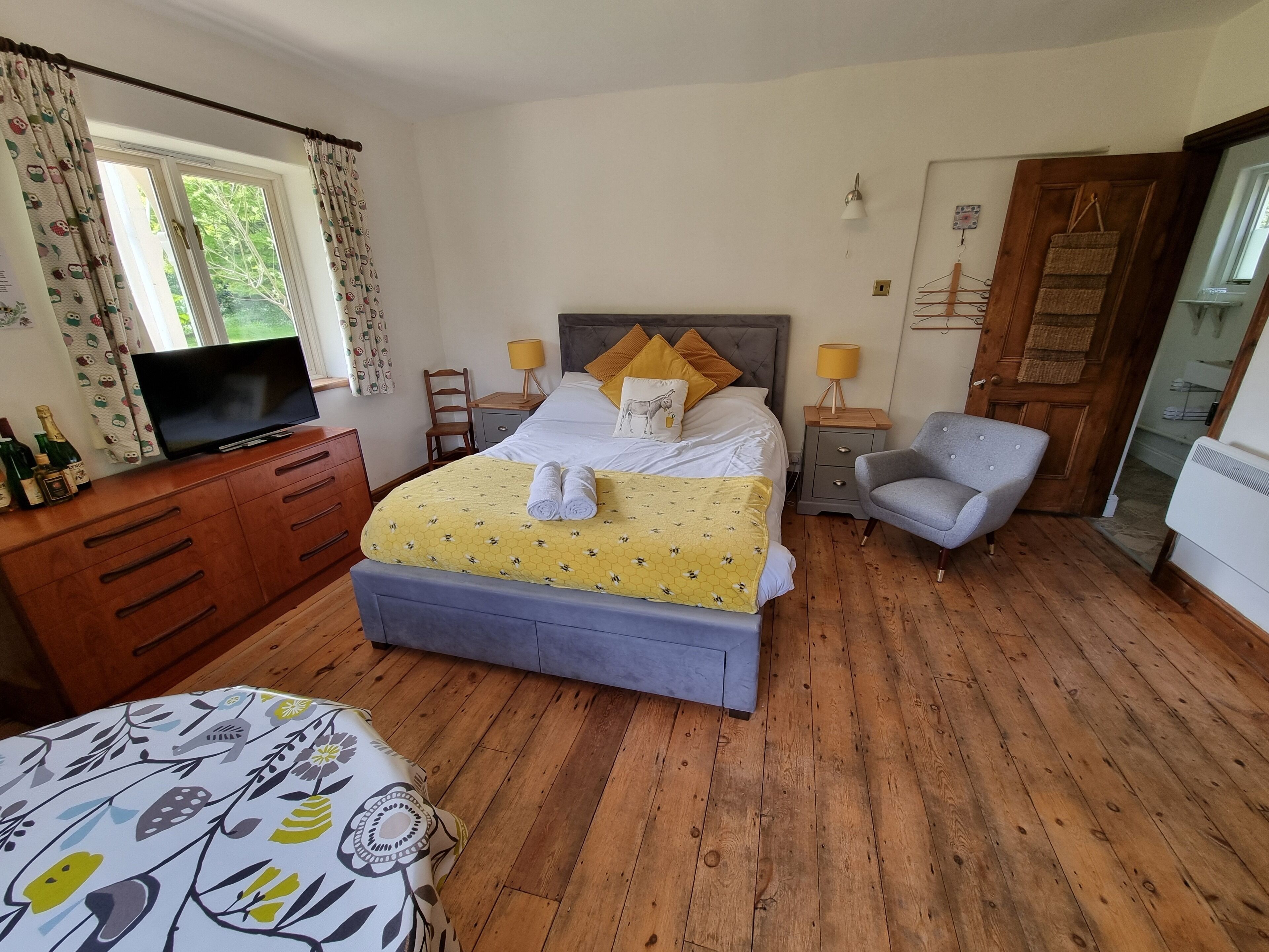 A neatly arranged bedroom with a bed, bedside tables, a chair, a television, and a wooden dresser.