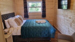 A cozy wooden room with a bed, a nightstand, a chair, and a window with curtains.
