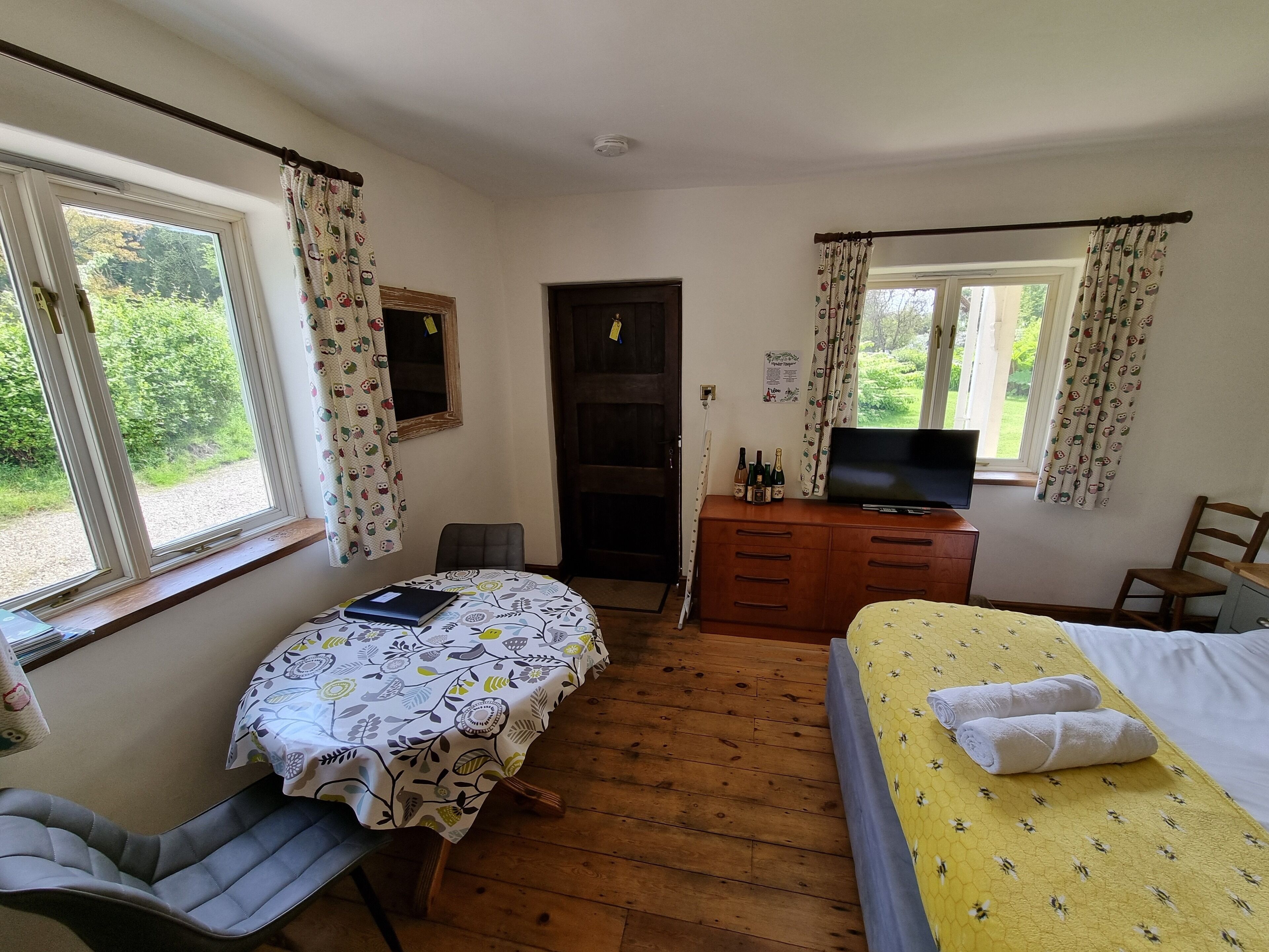 A room with a bed, a desk with a TV, a chair, and a window with curtains.